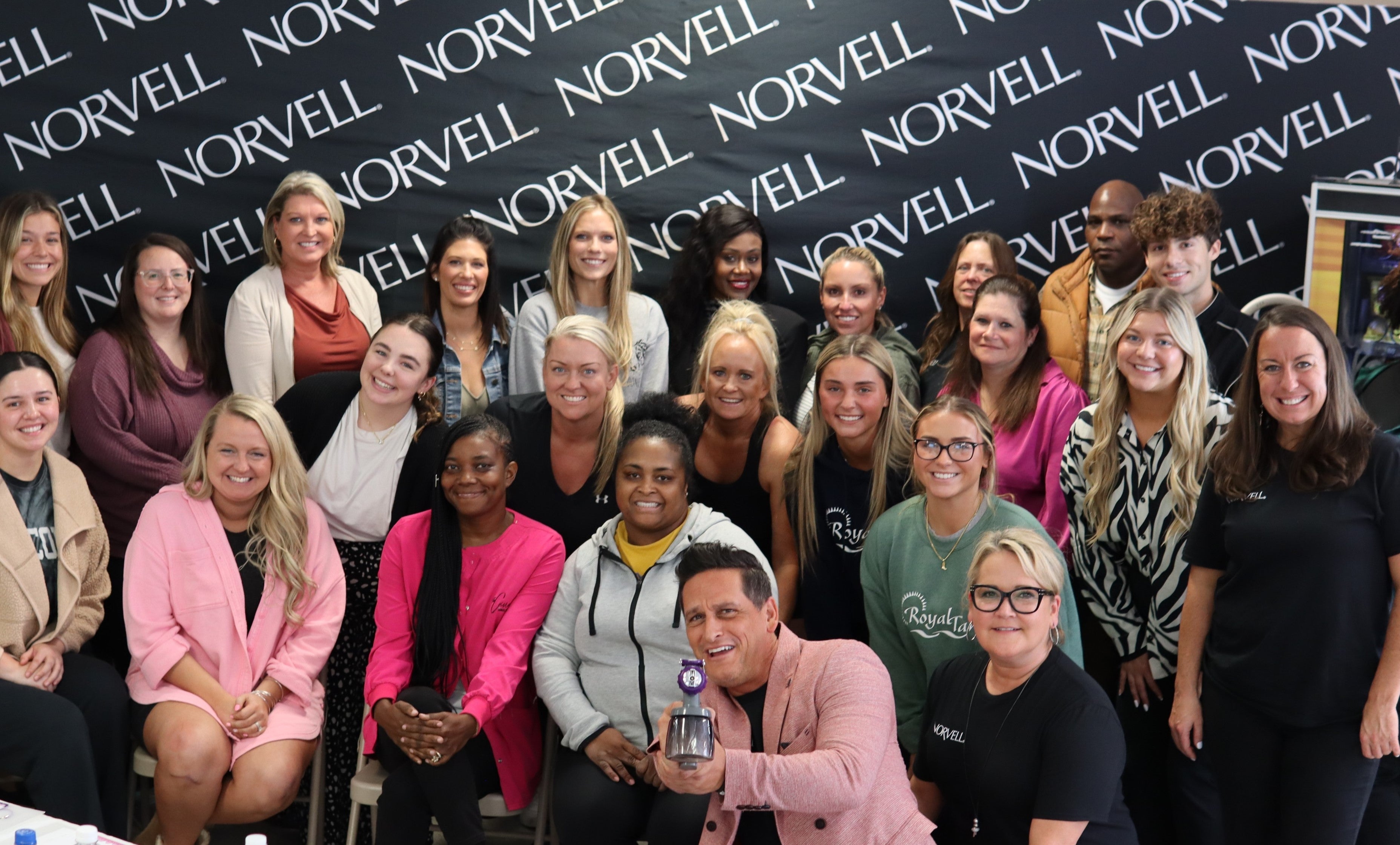 Brandon holds a Norvell M1000 spray tan system with a group of class attendees.