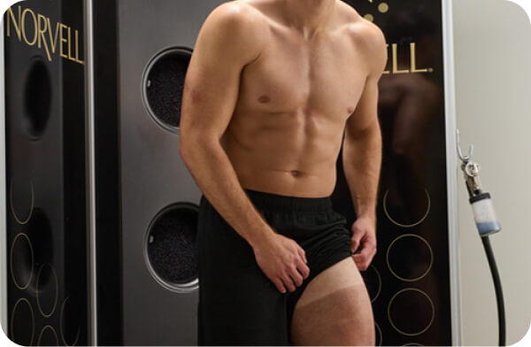 Male model showing before-and-after leg color inside the Norvell spray booth during training