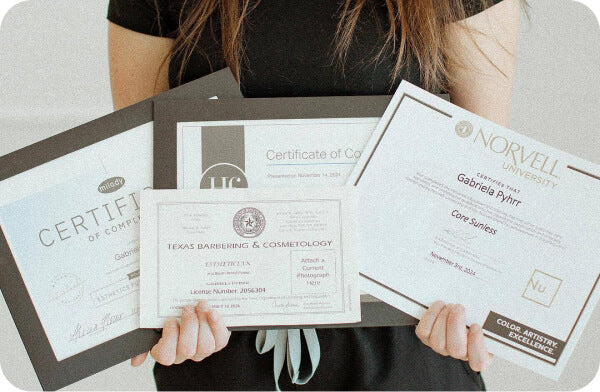 Student holding cosmetology and Norvell spray tan training certificates in Dallas