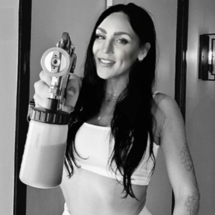 Jackie holding a Norvell Spray Tan Gun machine in a black and white photo