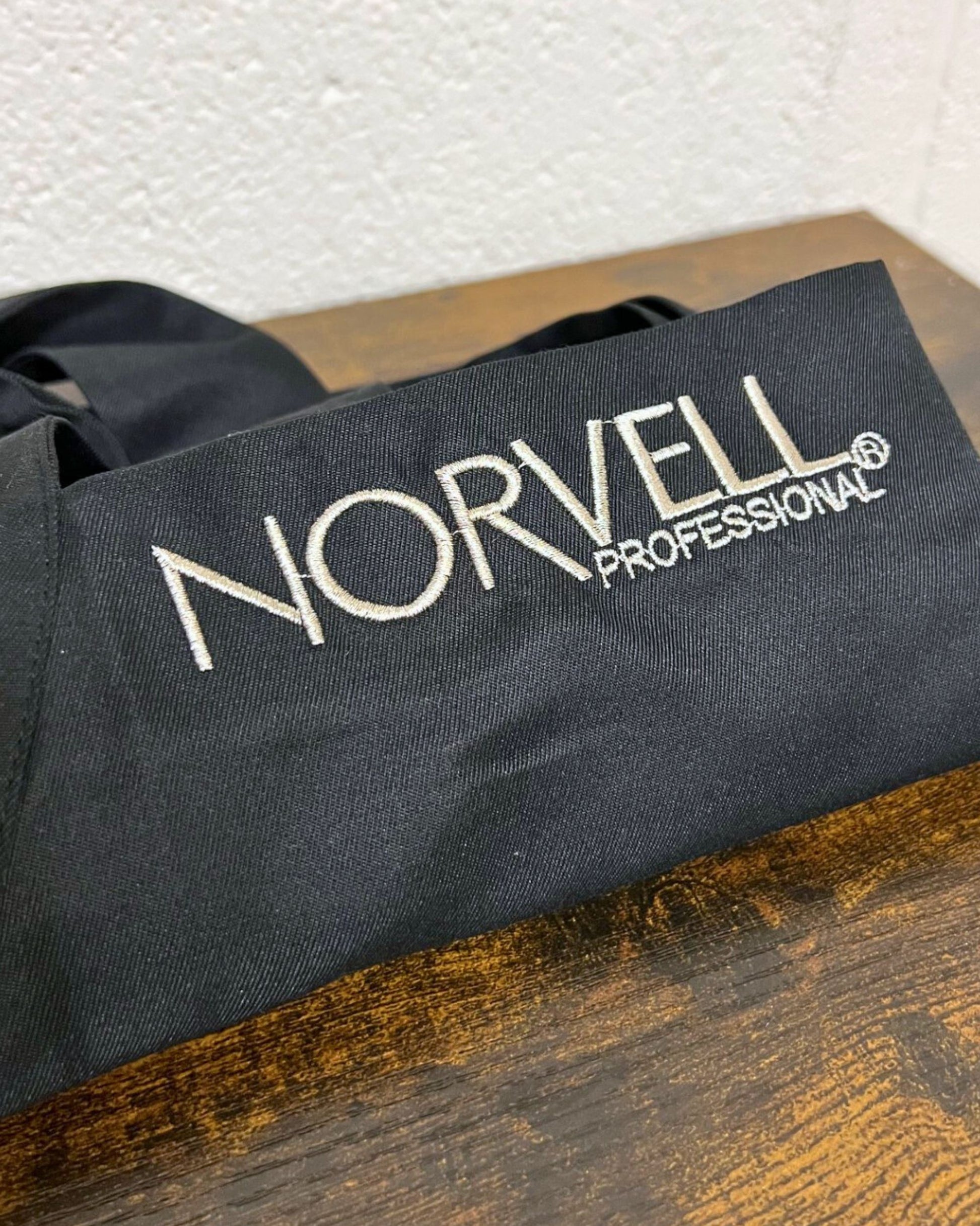 Black apron with an embroidered Norvell logo, on a wooden surface