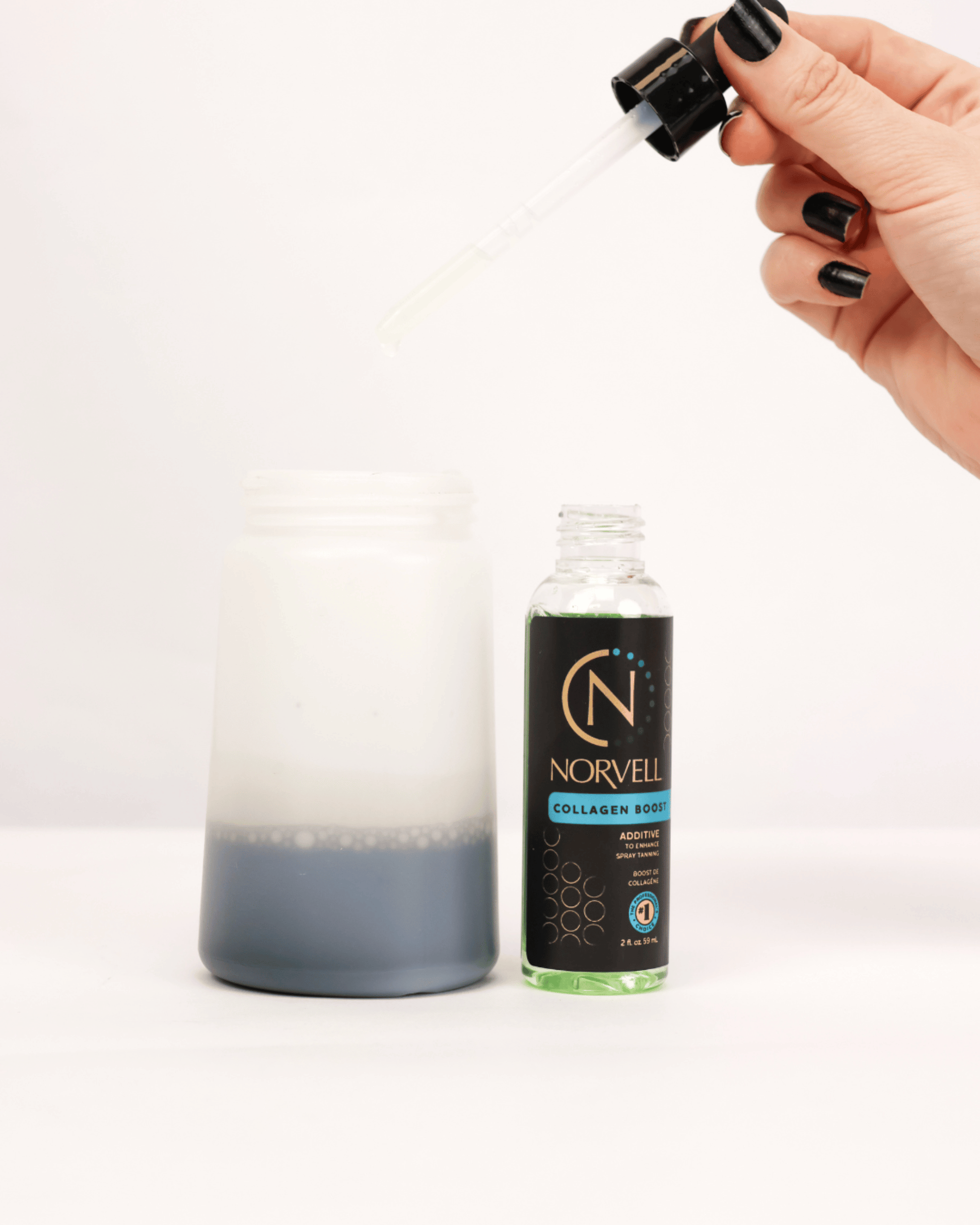 A hand with black nail polish holds a dropper above a solution cup adding Norvell Collagen Boost drops to Norvell Spray Tan solution in a solution cup.