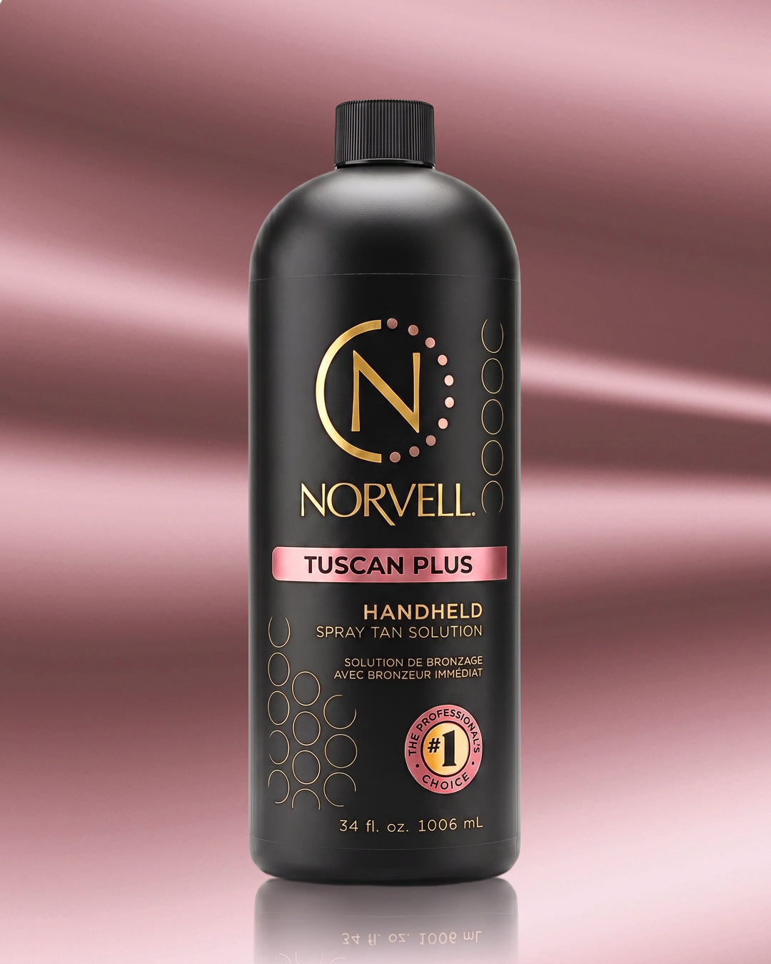 A bottle of Norvell Tuscan Plus Handheld Spray Tan Solution, featuring a matte black bottle with gold and pink accents, set against a pink gradient background with a soft reflection.