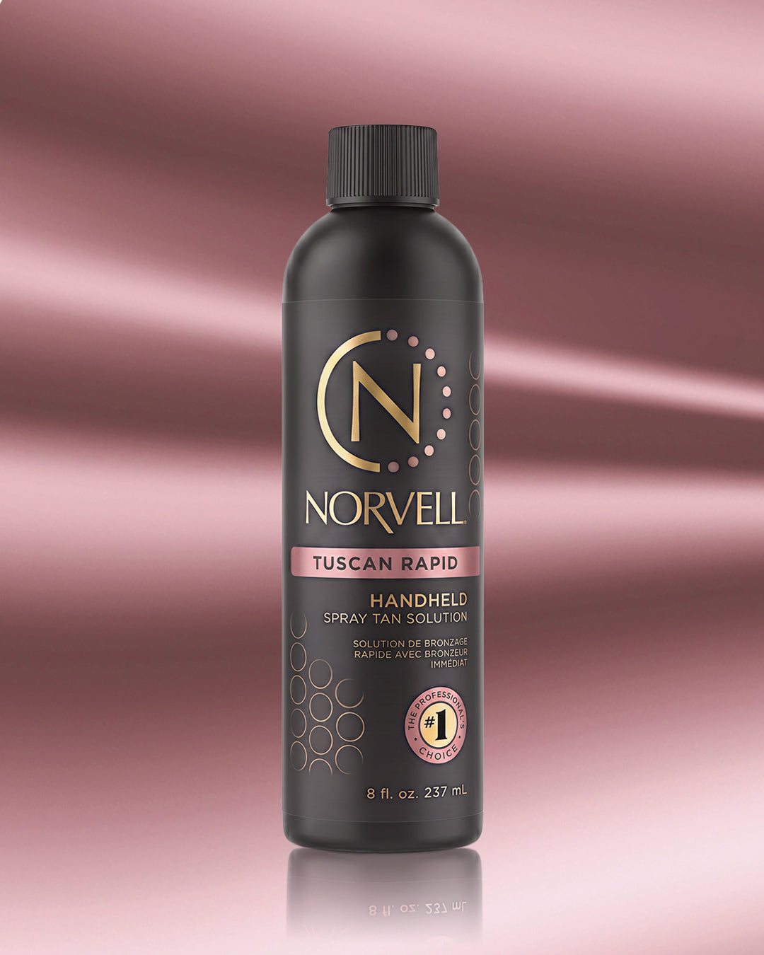 A bottle of Norvell Tuscan Rapid Handheld Spray Tan Solution, featuring a matte black bottle with gold and pink accents, set against a pink gradient background with a soft reflection.