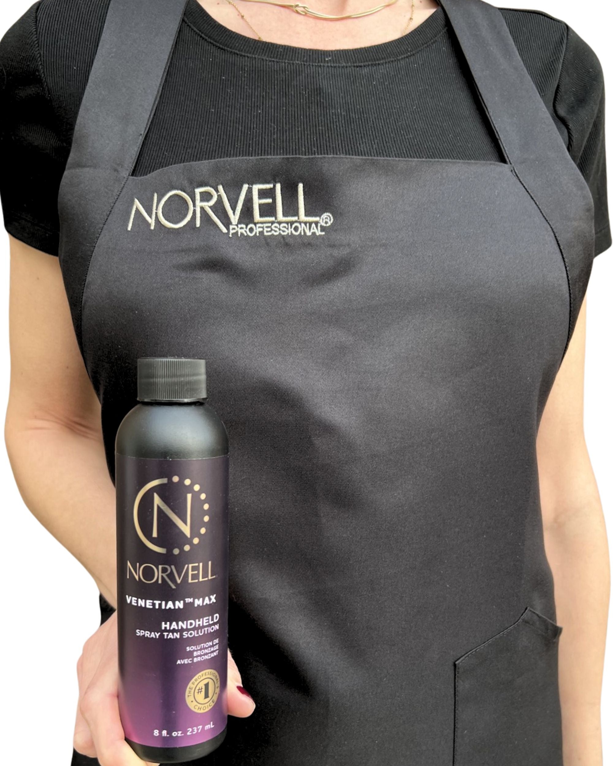 Person wearing a black apron with an embroidered Norvell logo, holding a Norvell tanning spray bottle, in front of a white background