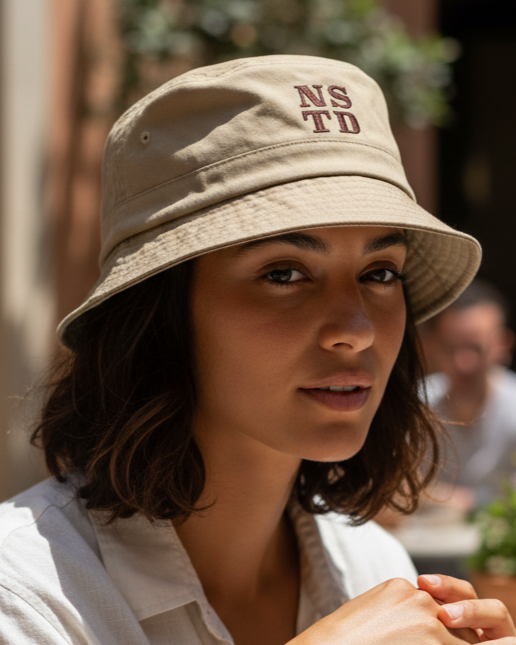 AI Render Woman wearing a beige bucket hat with 'NSTD' text, sitting outdoors.