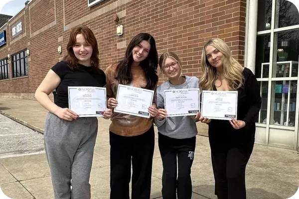 Four women holding Norvell spray tan certification certificates outside a training facility.