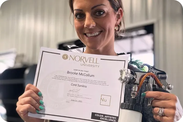 Woman holding Norvell University Core Sunless spray tan certification with airbrush equipment.